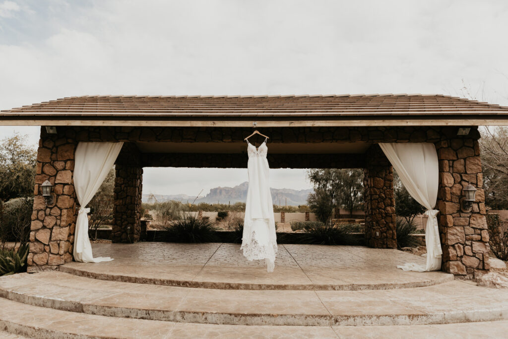 Wedding dress hanging up at the alter. The alter is stone with two curtains on either side. The Superstition Mountains are visible in the background.
