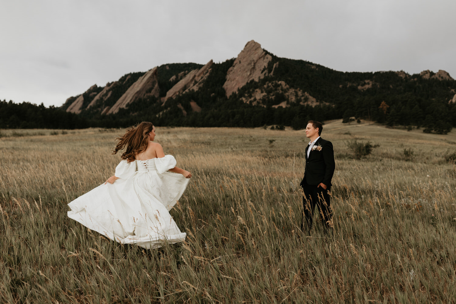 Groom watches his bride spin around in her dress in the meadows of Chautauqua Park. The Flatirons are visible in the distance.